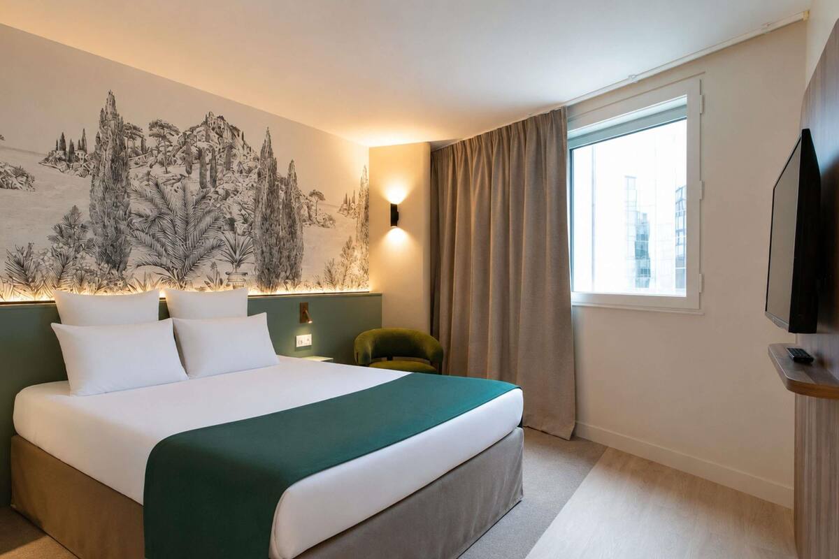 A hotel room with a bed, a wall mural, a window, and a television.