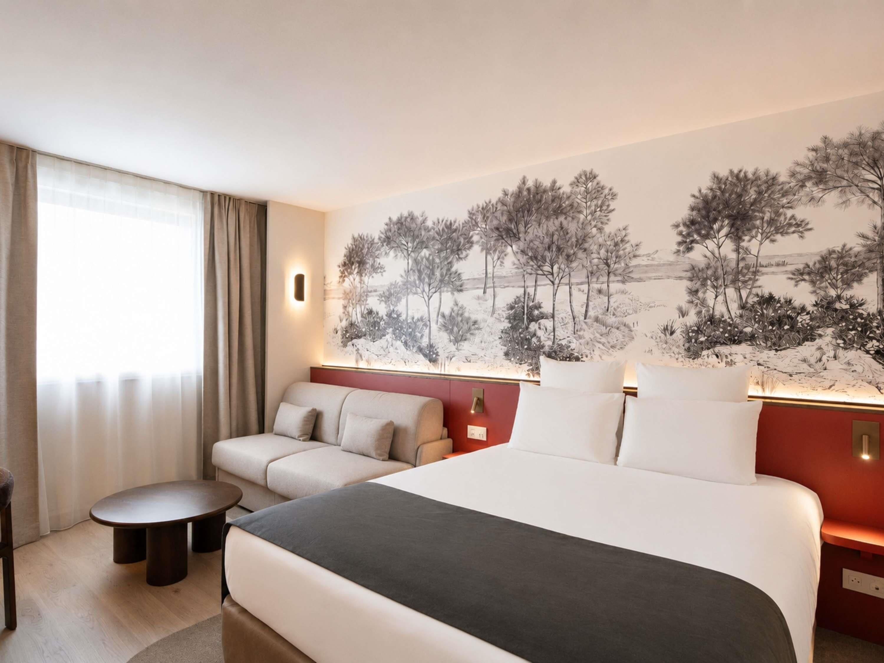 Habitación de hotel con cama, sofá, una mesita y una lámpara de pared.