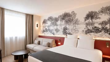 Habitación de hotel con cama, sofá, una mesita y una lámpara de pared.