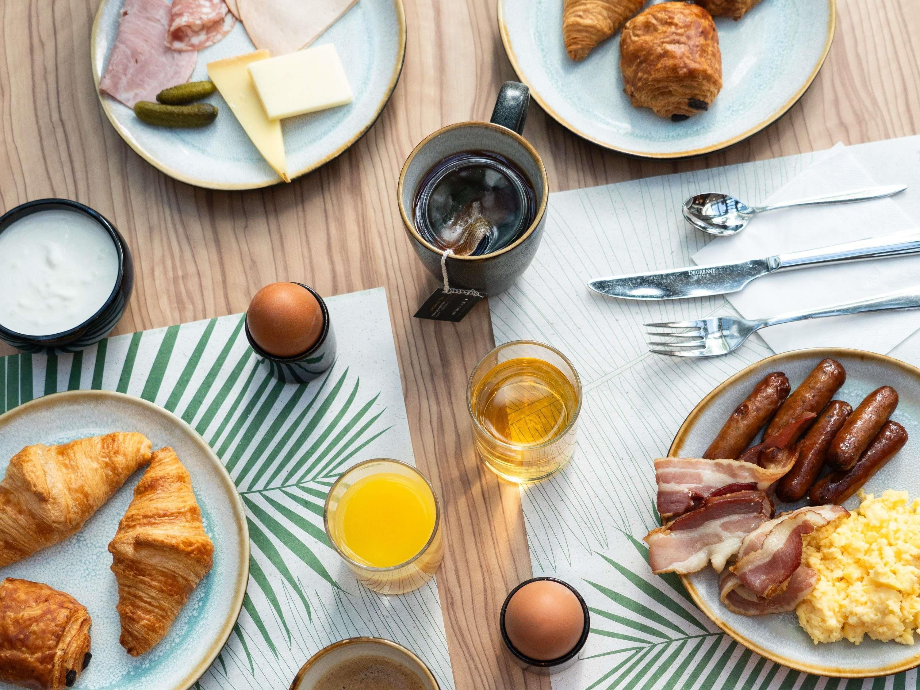 A breakfast table with croissants, sausages, eggs, and juice.