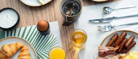 A breakfast table with croissants, sausages, eggs, and juice.