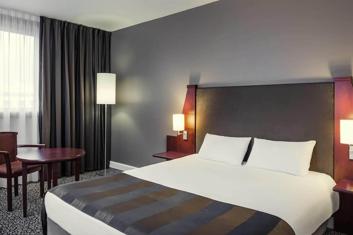 Habitación de hotel con una cama grande, un escritorio, una silla y una lámpara.