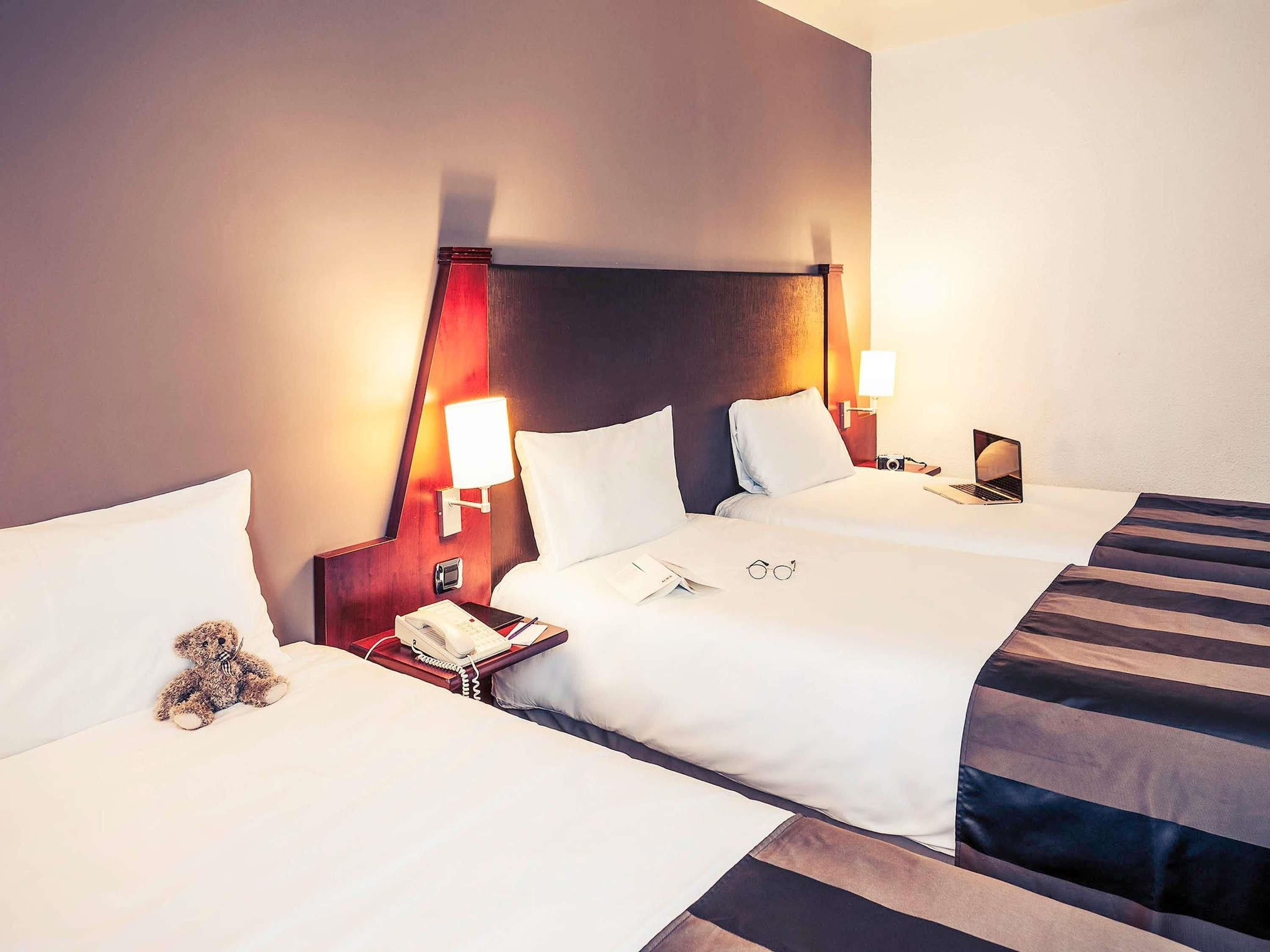 A hotel room with two beds, bedside lamps, a telephone, and a teddy bear on one bed.