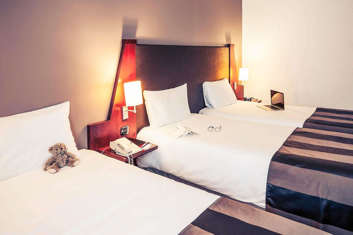 A hotel room with two beds, bedside lamps, a telephone, and a teddy bear on one bed.