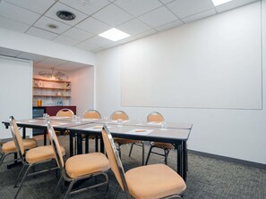 A conference room with a large table, chairs, a projector screen, and a bookshelf in the background.