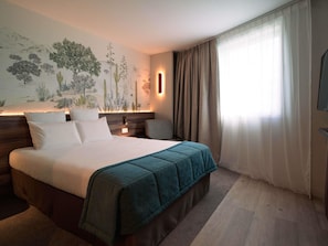 A hotel room with a bed, a nightstand, a wall-mounted TV, and a large window with curtains. - Mercure Paris Val de Fontenay (Fontenay-sous-Bois)