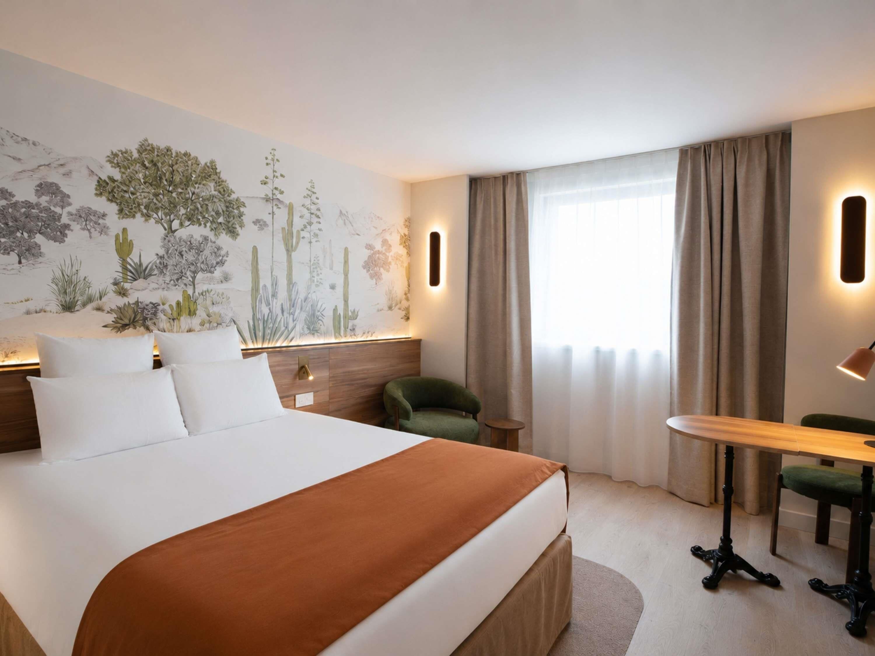 A hotel room with a large bed, a desk, a chair, a nightstand, and a wall mural.