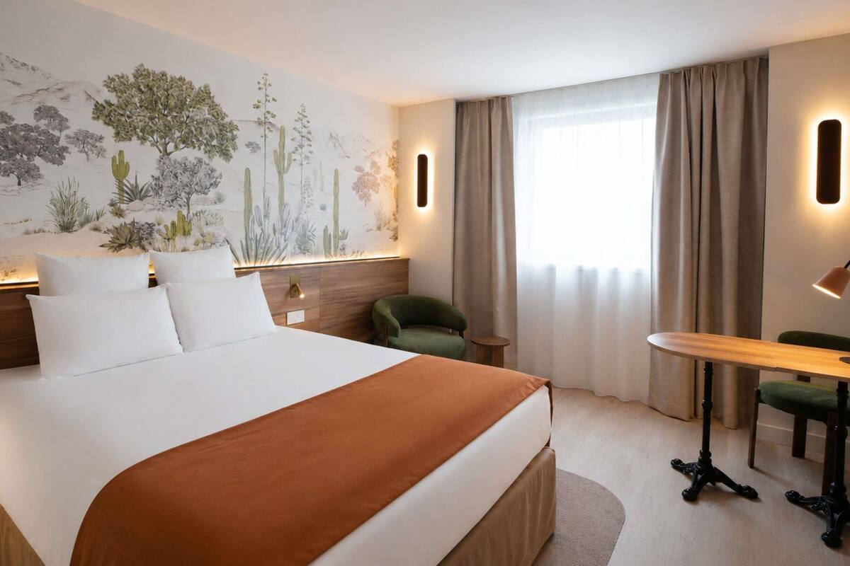 A hotel room with a large bed, a desk, a chair, a nightstand, and a wall mural.