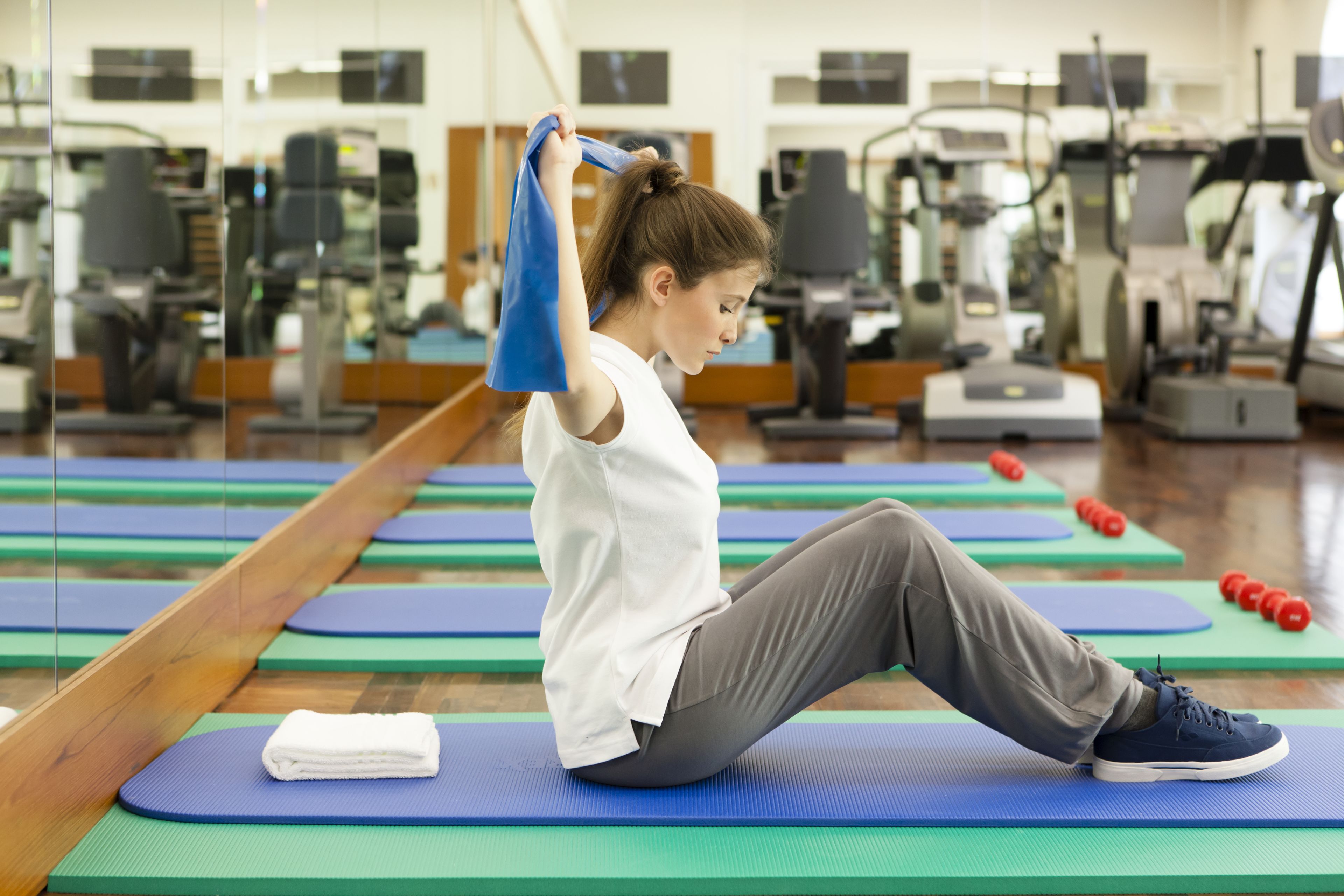 Una persona si allena su un tappetino blu in palestra, sullo sfondo si vedono diverse attrezzature.