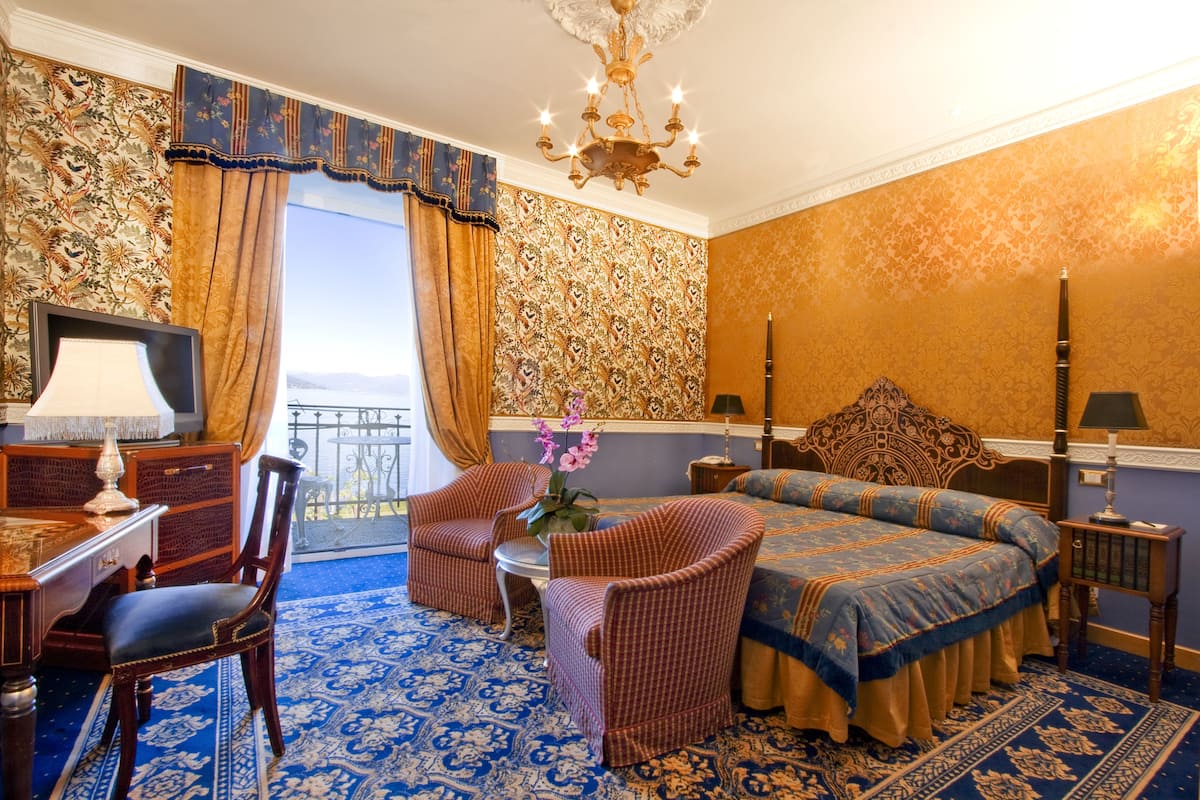 A hotel room with a large bed, two armchairs, a desk with a lamp, and a view of the sea.