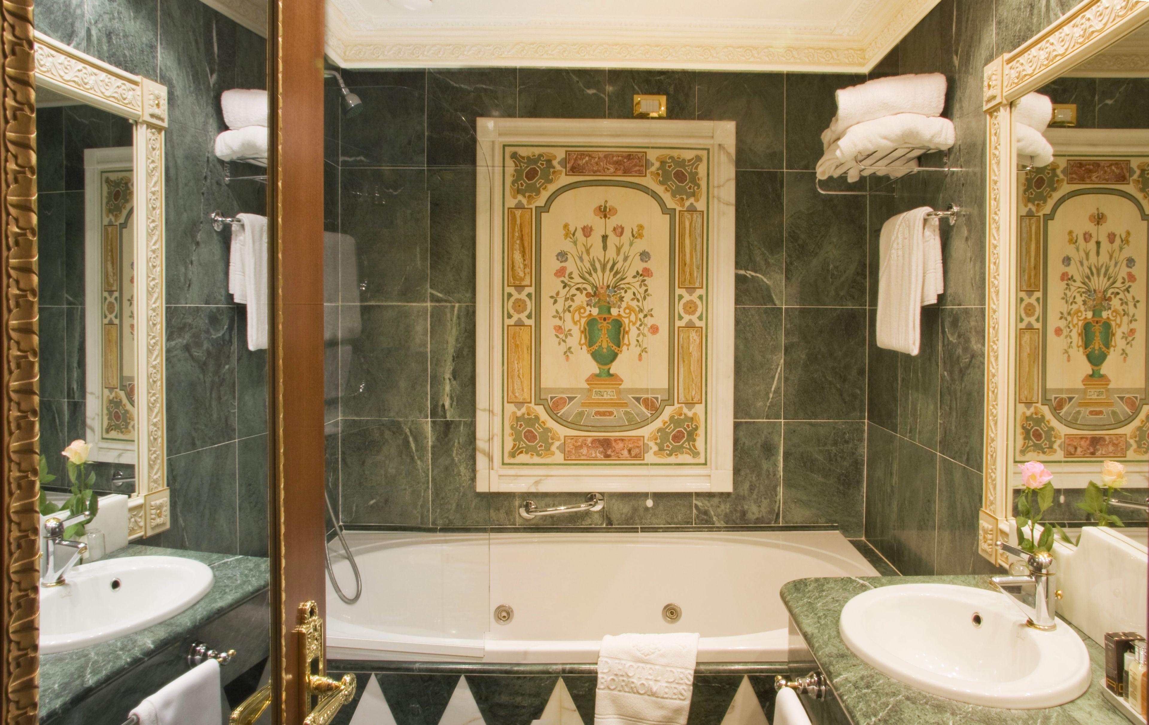 A luxurious bathroom with a large bathtub, two sinks, and ornate wall decorations.