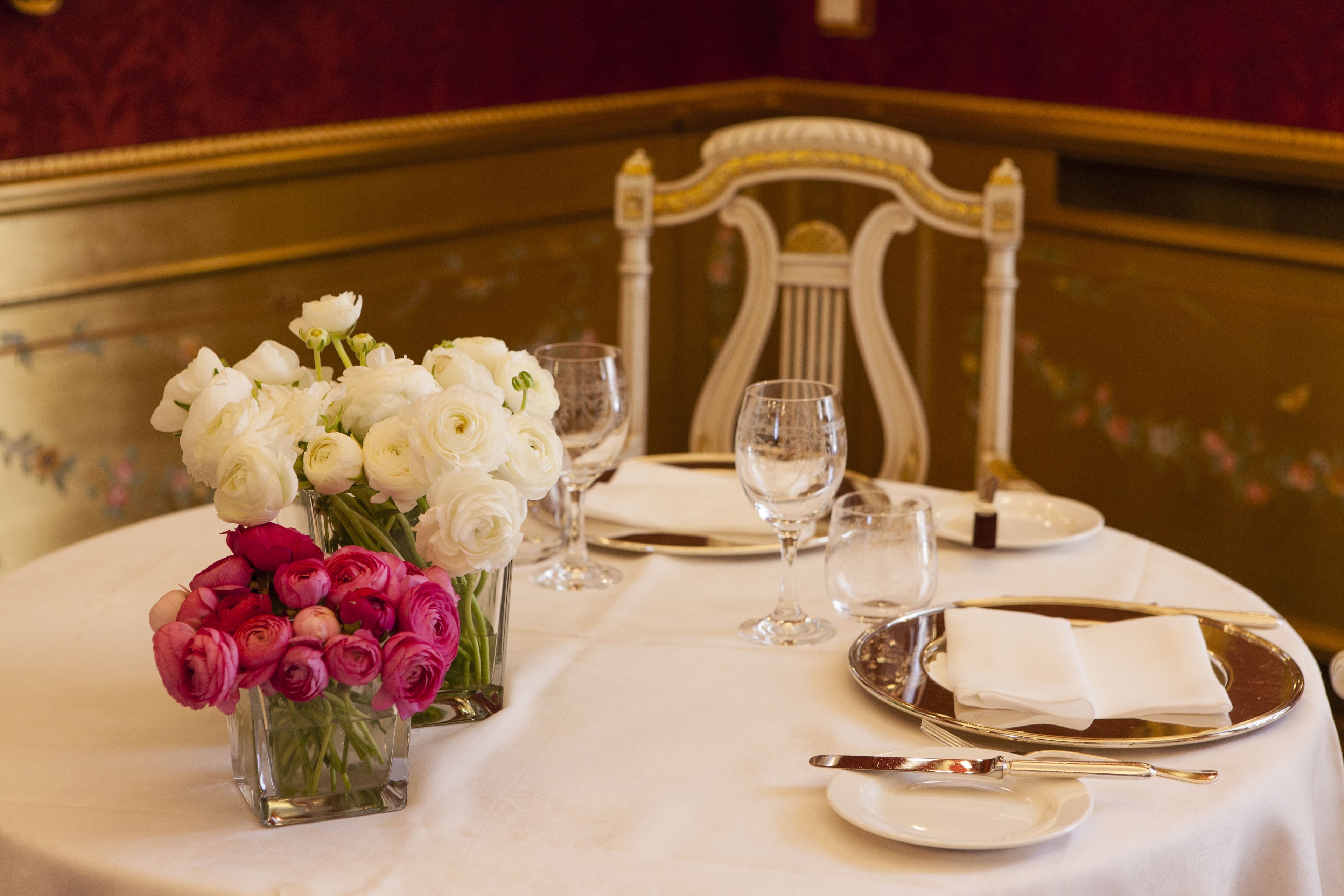 Mesa lista para comer con rosas blancas y rosadas, copas transparentes y cubiertos.