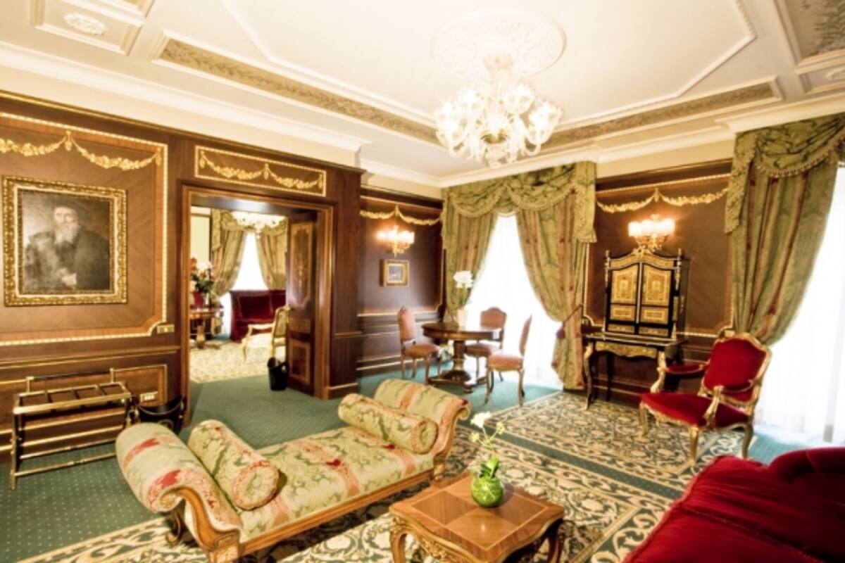 A room with a patterned carpet, a sofa, a red armchair, a wooden cabinet, and a chandelier.