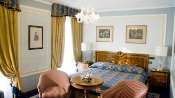Ein Hotelzimmer mit einem großen Bett, zwei Stühlen, einem runden Tisch und einer Kronleuchter.
