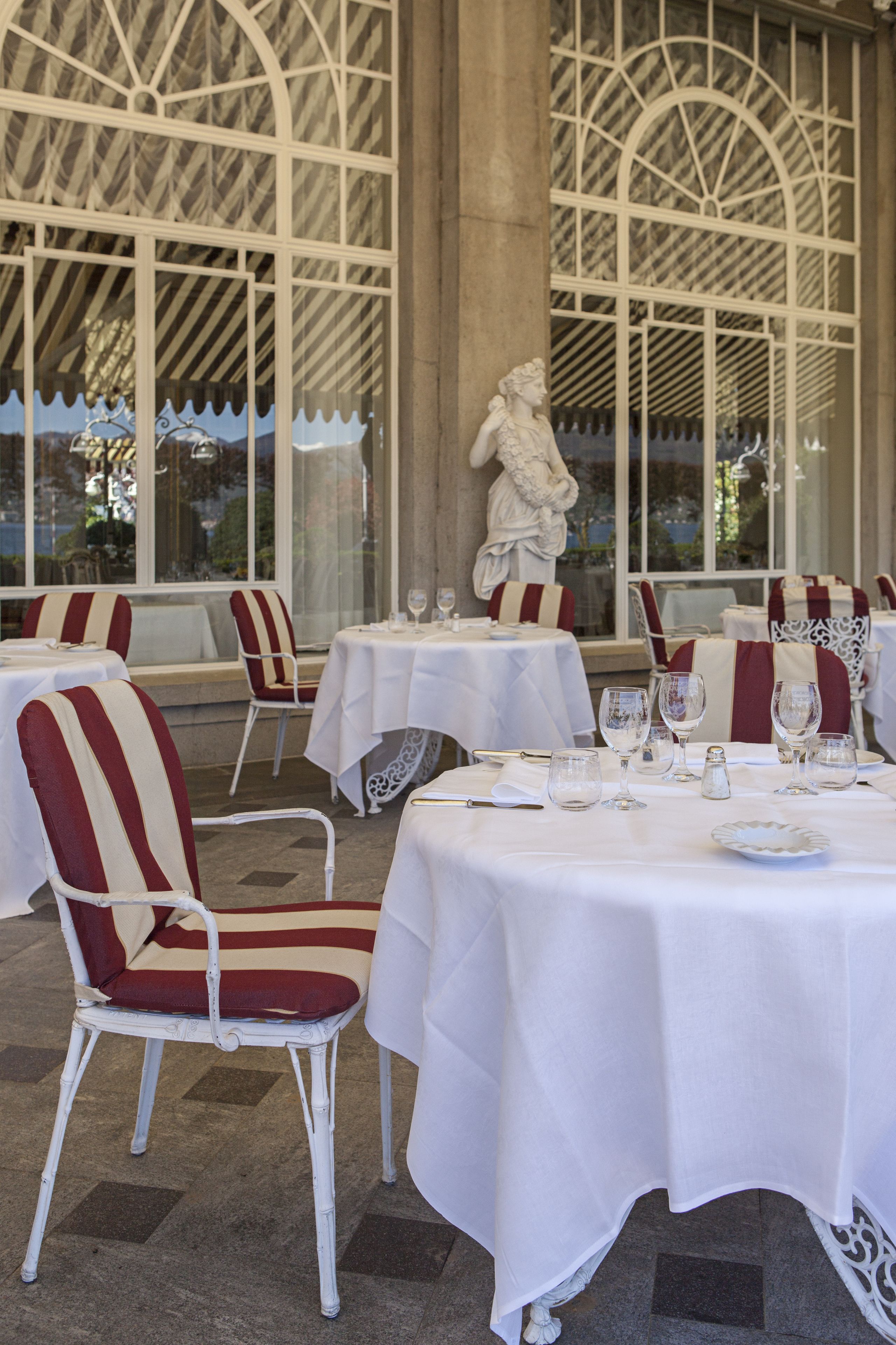 A restaurant with white tables and chairs, a statue, and a view through large windows.