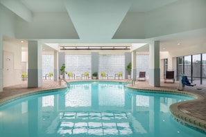 Una piscina interior con agua cristalina, rodeada de sillones de descanso y plantas en macetas.