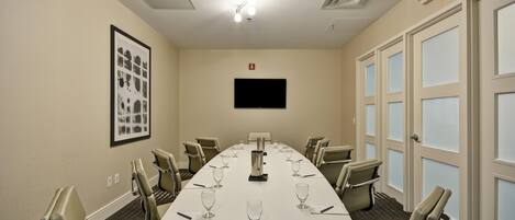 A conference room with a long table, chairs, a flat-screen TV, and an exit sign.