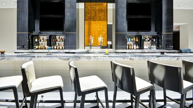 A bar area with a tiled backsplash, bar stools, and a variety of bottles. - Embassy Suites Hotel Charlotte (Charlotte)