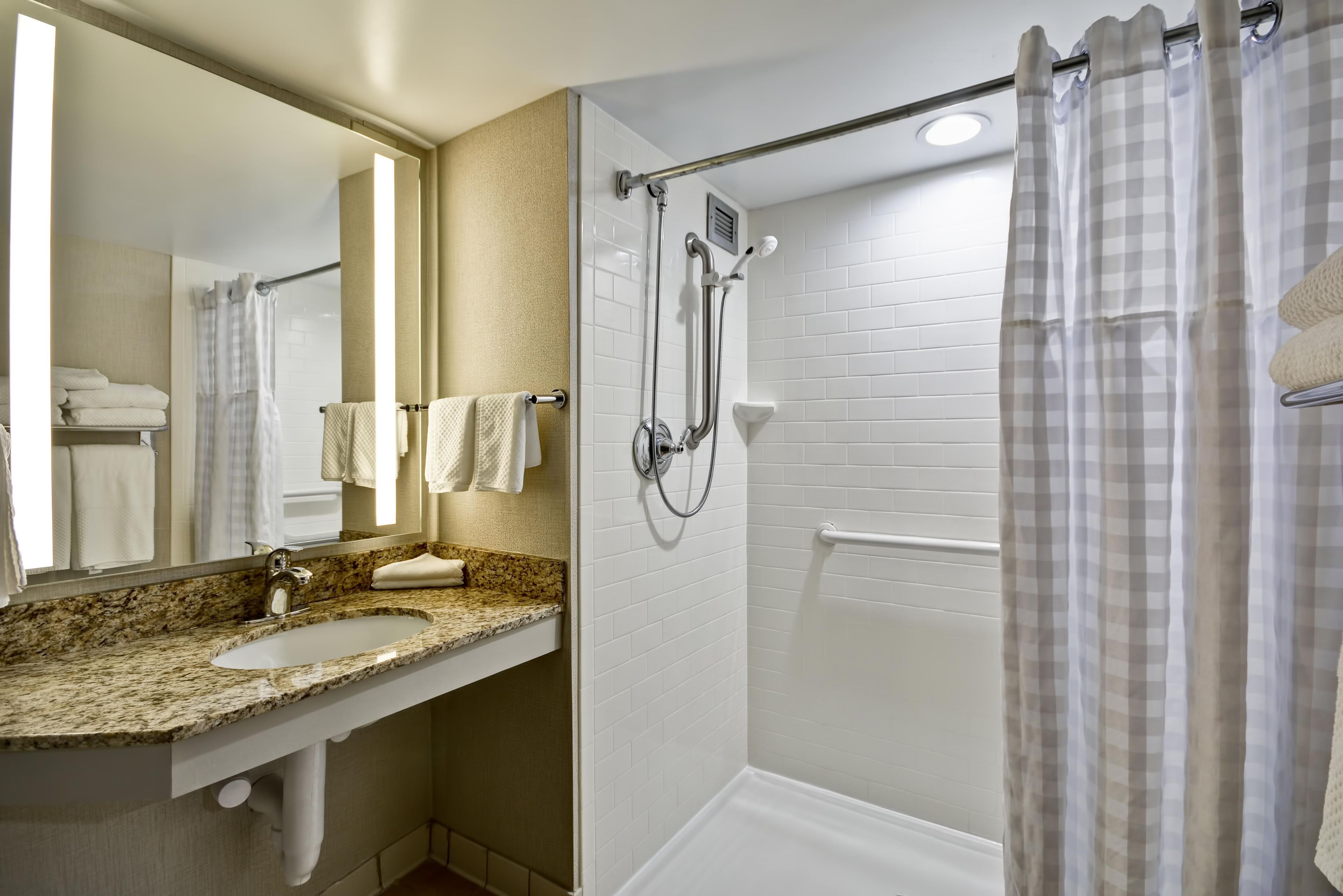 A bathroom with a granite countertop sink, a mirror, a shower with a glass door, and a towel rack.