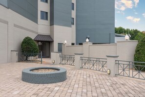 A courtyard with a circular brick firepit, a gated entrance, and a modern building with grey and white walls. - Embassy Suites Hotel Charlotte (Charlotte)