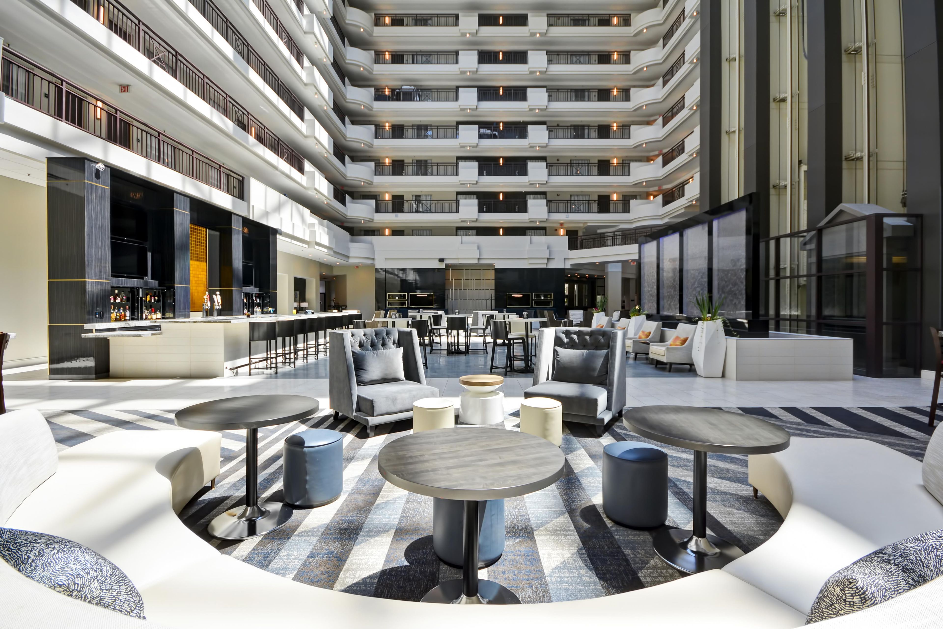 A spacious atrium with multiple seating areas, a bar, and a high ceiling with balconies.