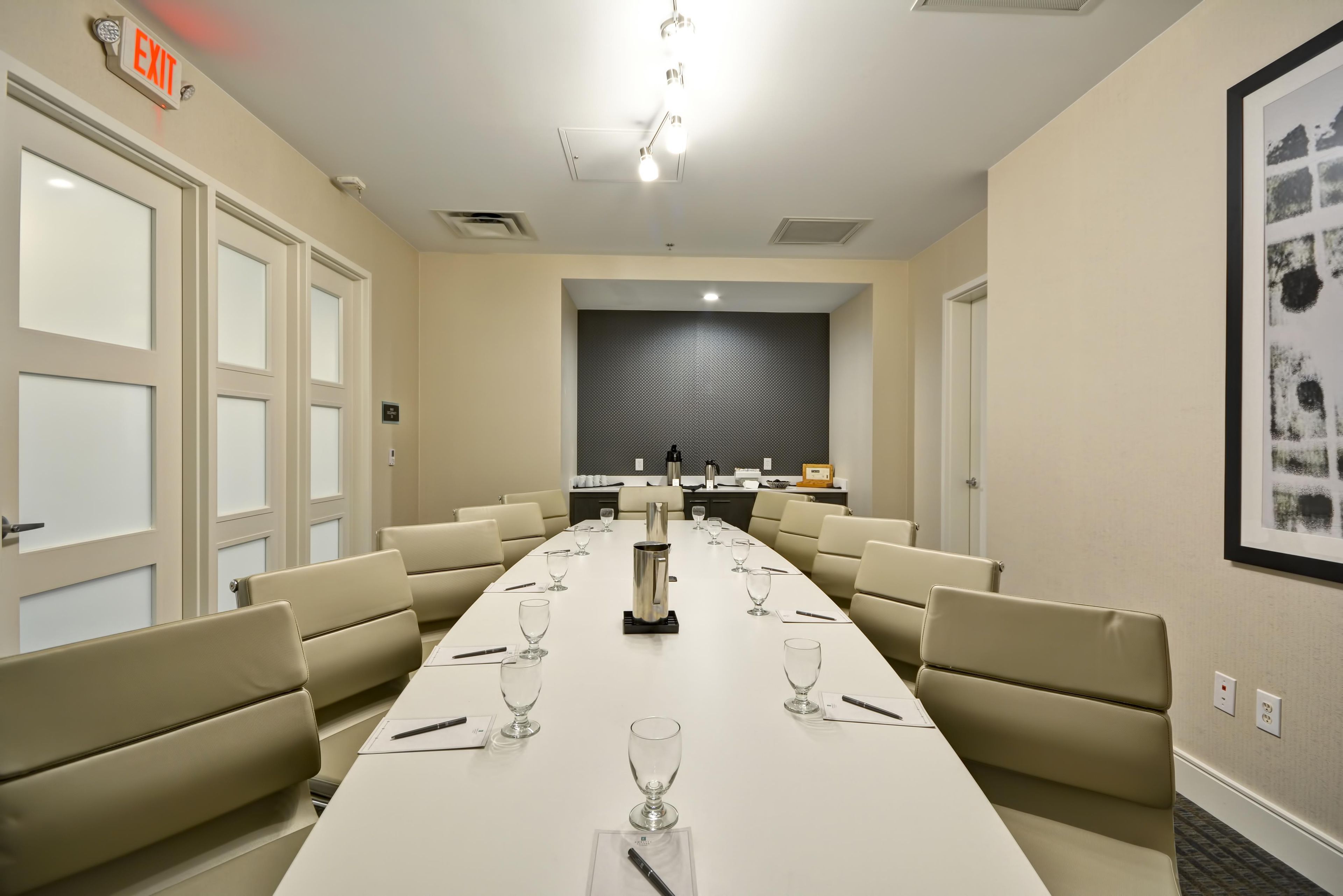 Un salón de conferencias con una larga mesa, sillas y una cocina al fondo.
