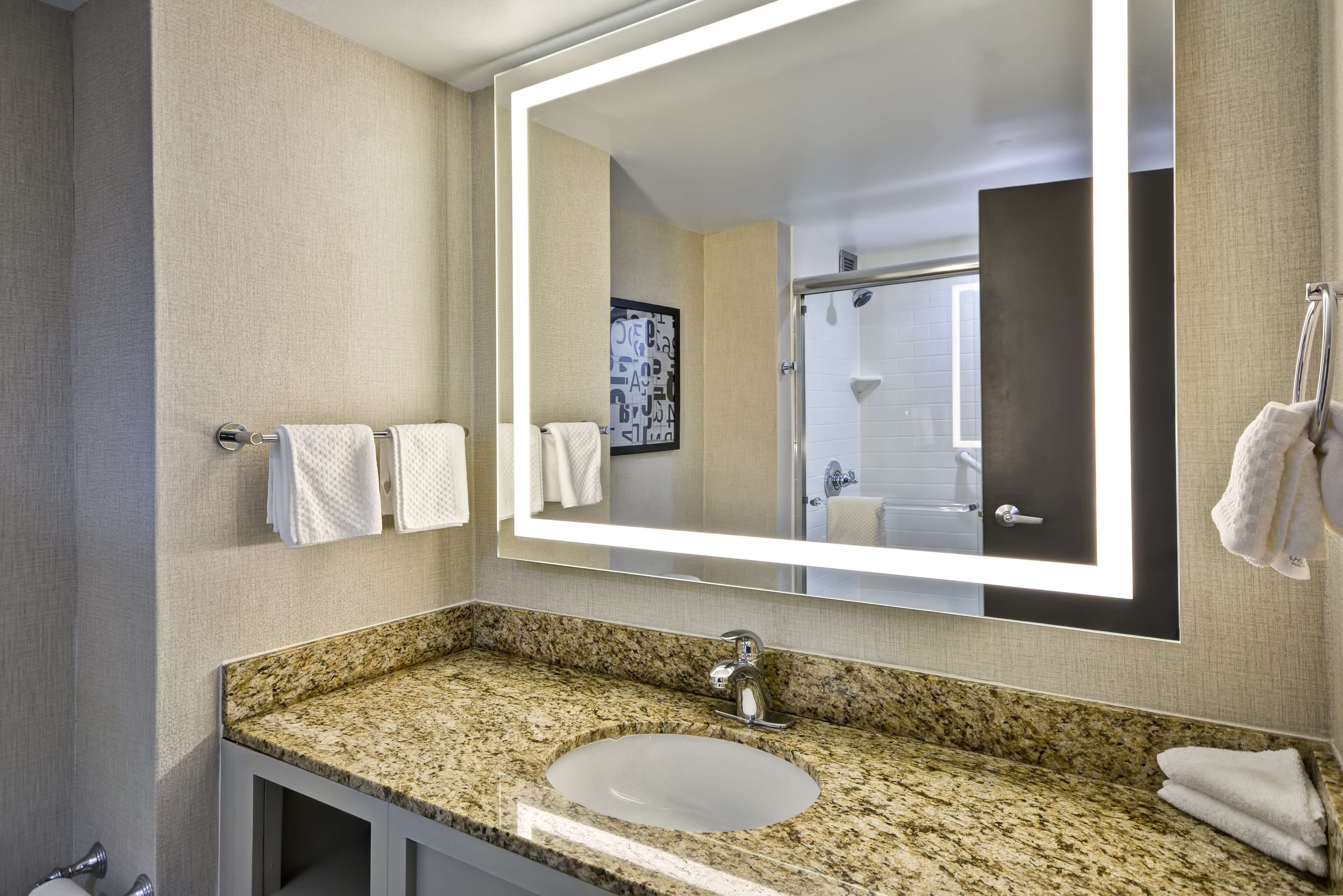 A bathroom with a granite countertop, a white sink, and a large mirror.