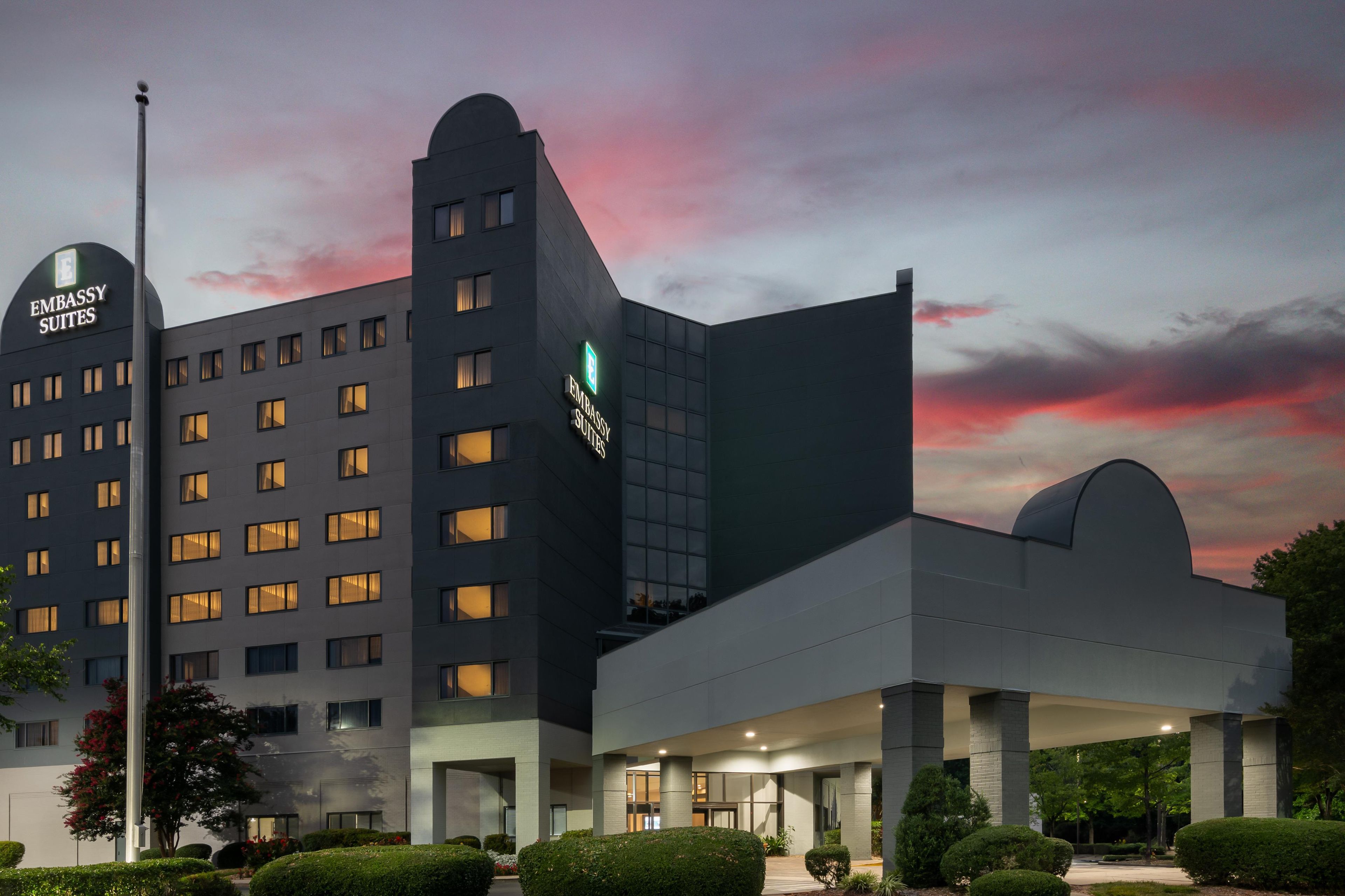 A modern building with multiple floors, a prominent sign for 'Embassy Suites,' and a well-lit entrance area.