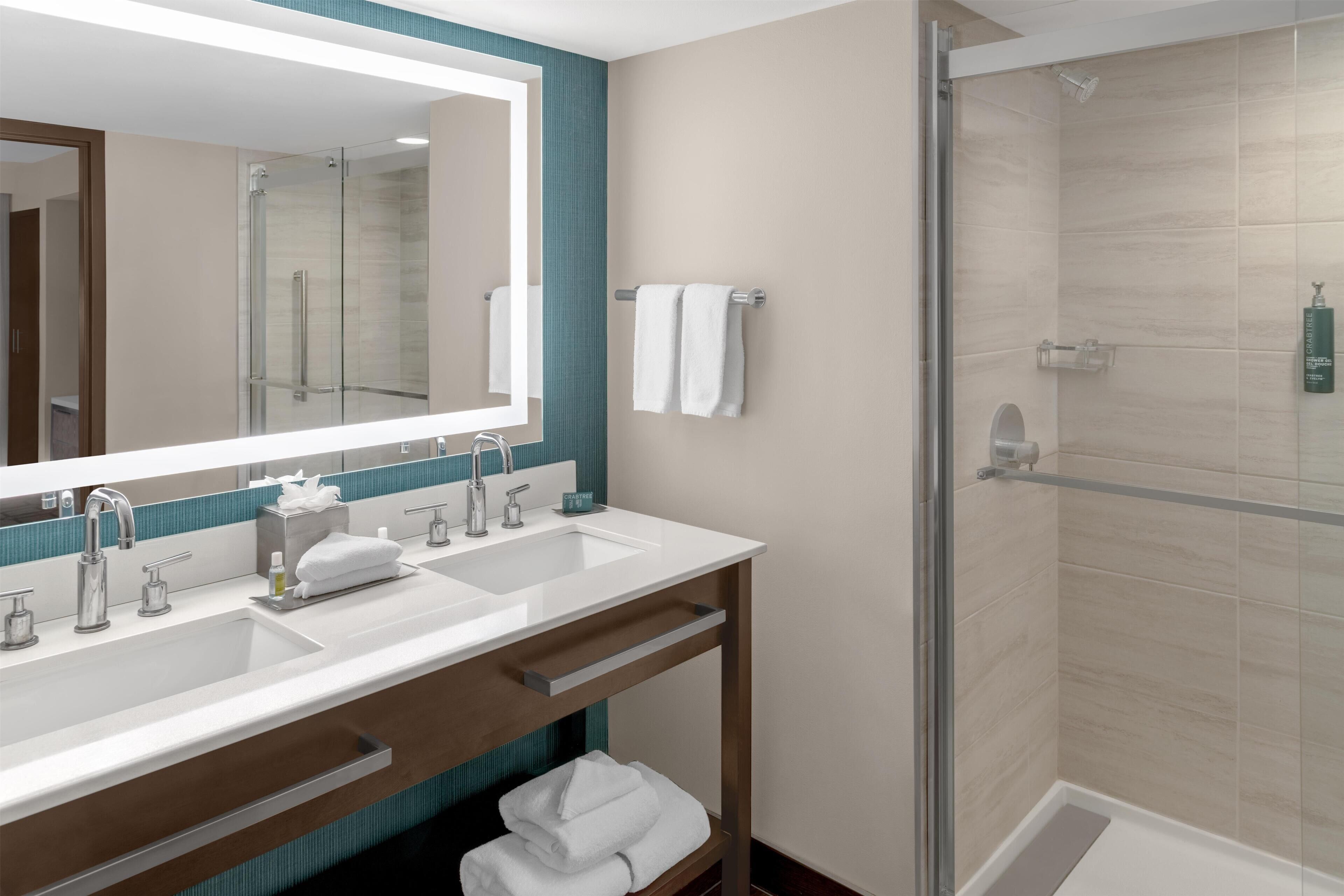 A modern bathroom with two sinks, a large mirror, and a glass-enclosed shower.