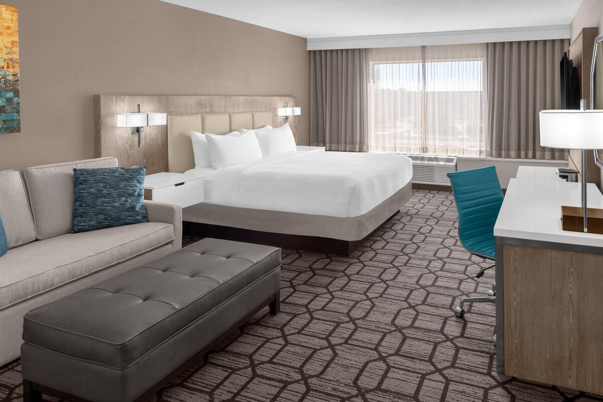 A hotel room with a bed, a sofa, a desk, and a chair.