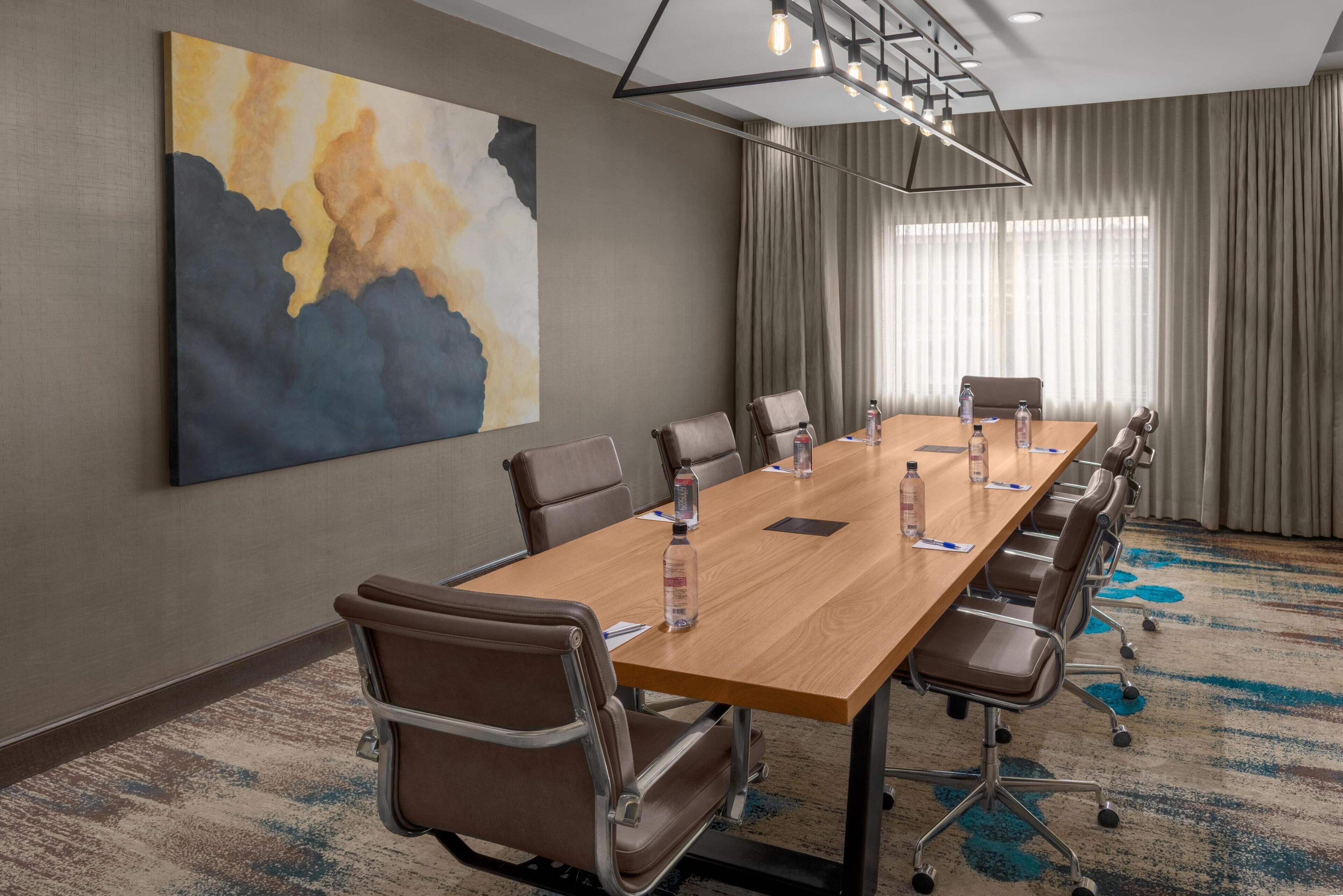 A conference room with a long table, chairs, a painting, and a modern chandelier.