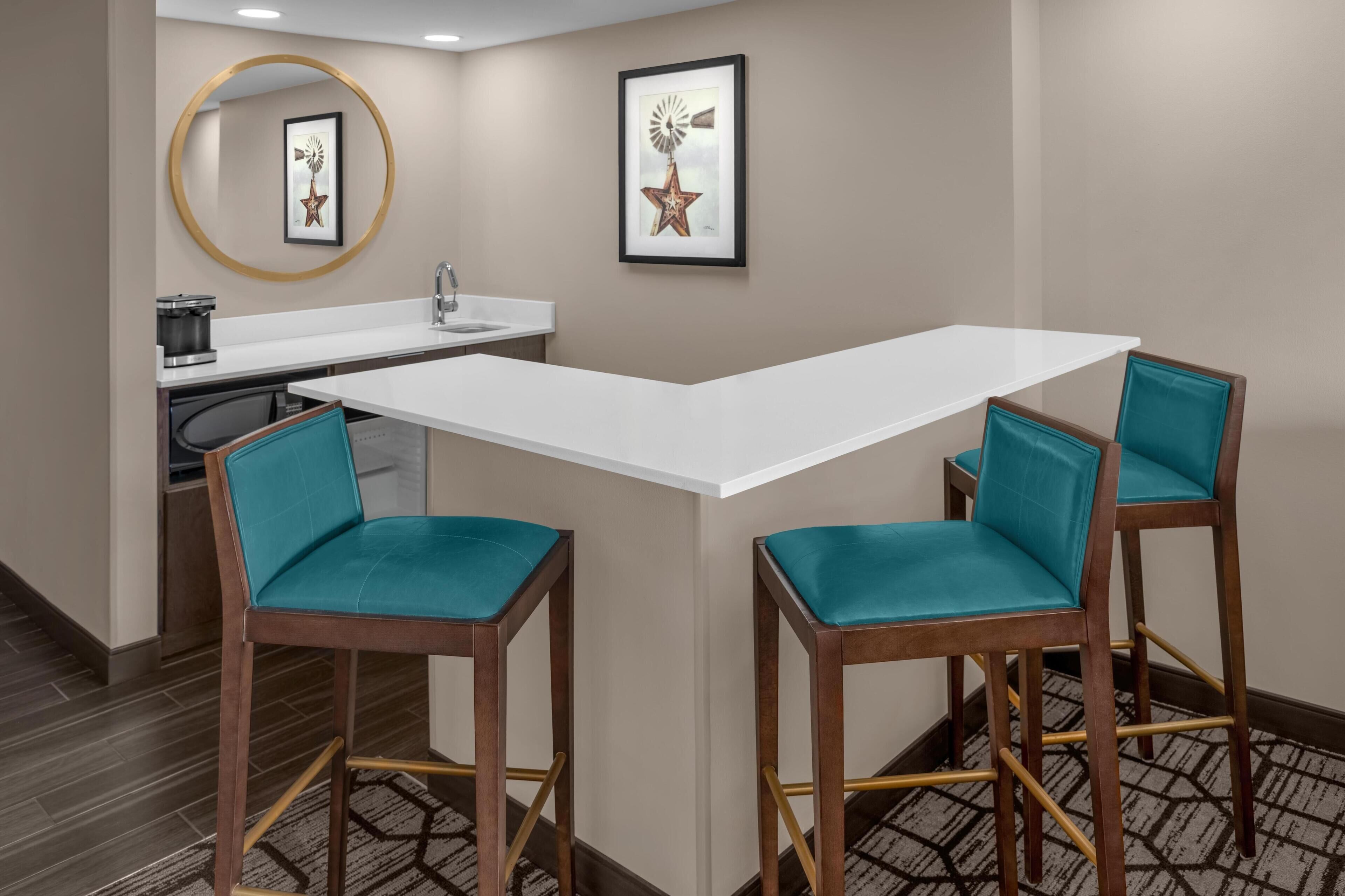 A corner seating area with a white table and two teal chairs, a sink, and a framed picture on the wall.