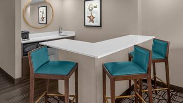 A corner seating area with a white table and two teal chairs, a sink, and a framed picture on the wall.