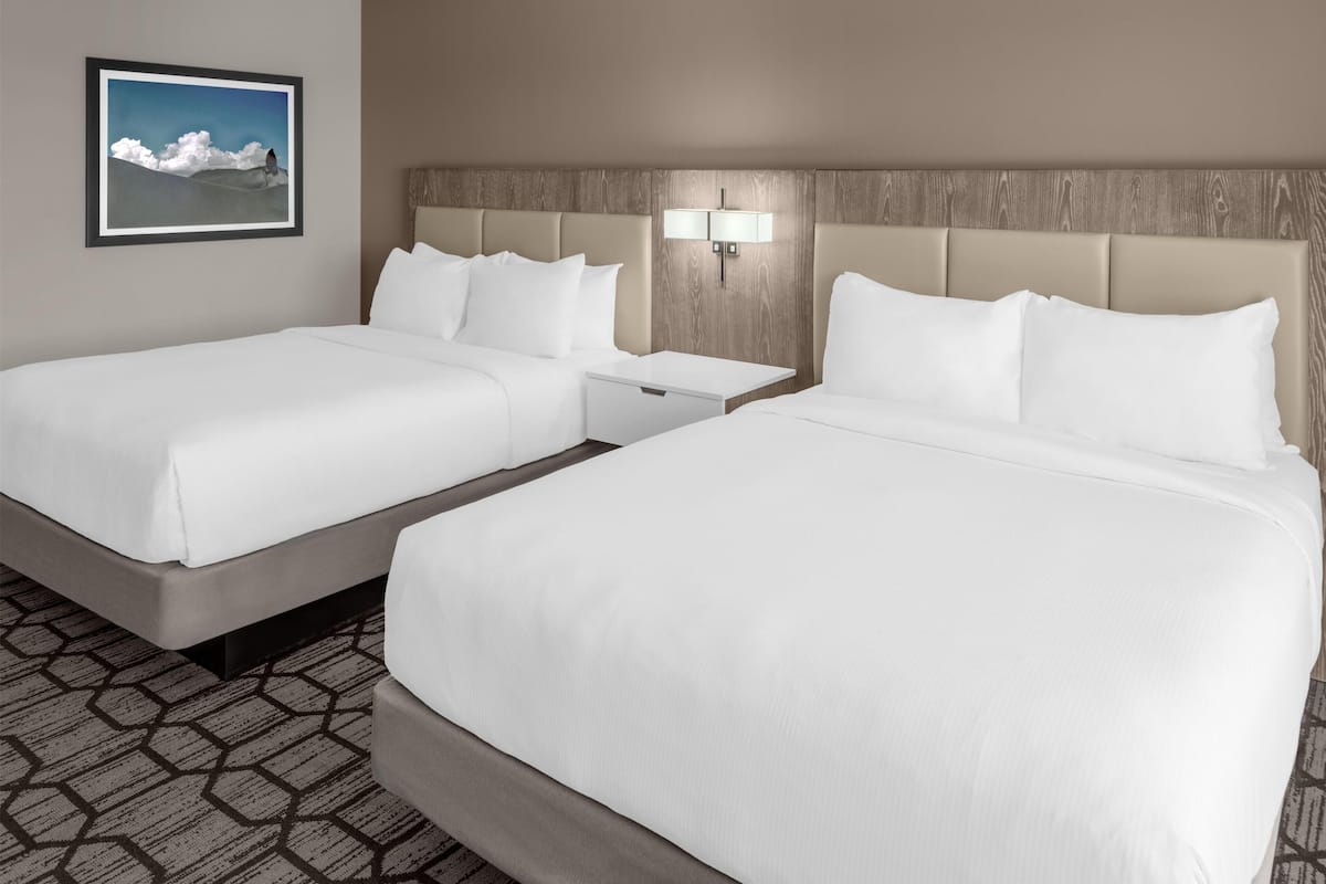 A hotel room with two beds, a nightstand, a wall-mounted lamp, and a framed picture.