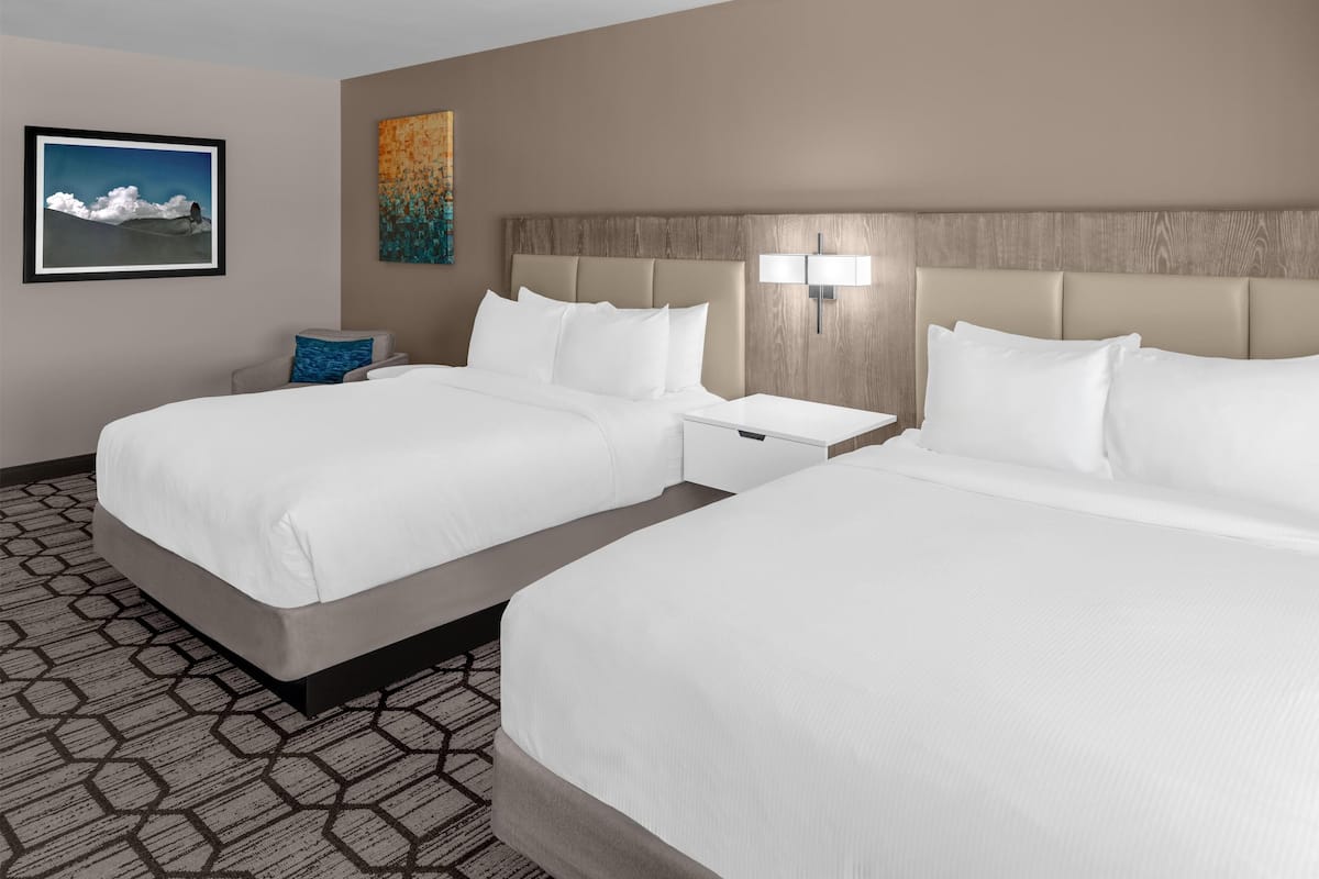 A hotel room with two beds, a nightstand, a lamp, a framed picture, and a patterned carpet.