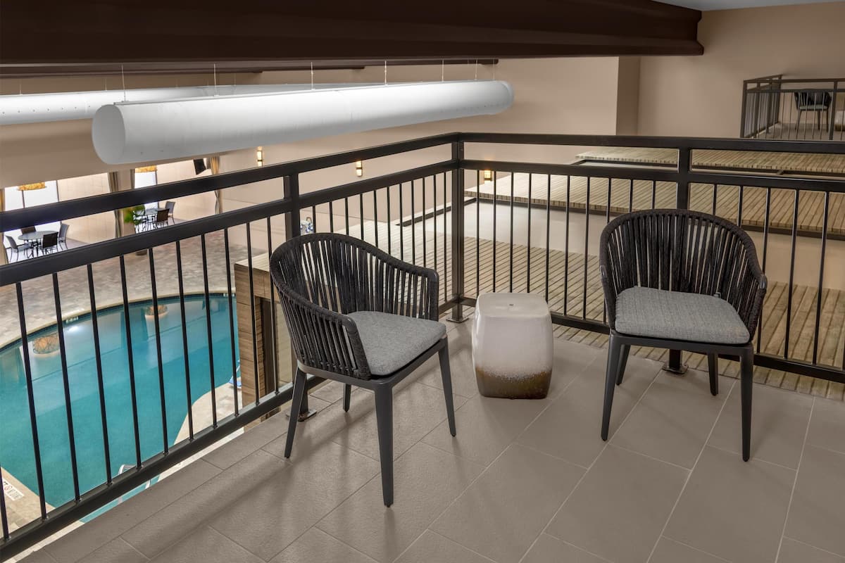 A balcony with two wicker chairs, a small ottoman, and a pool view.