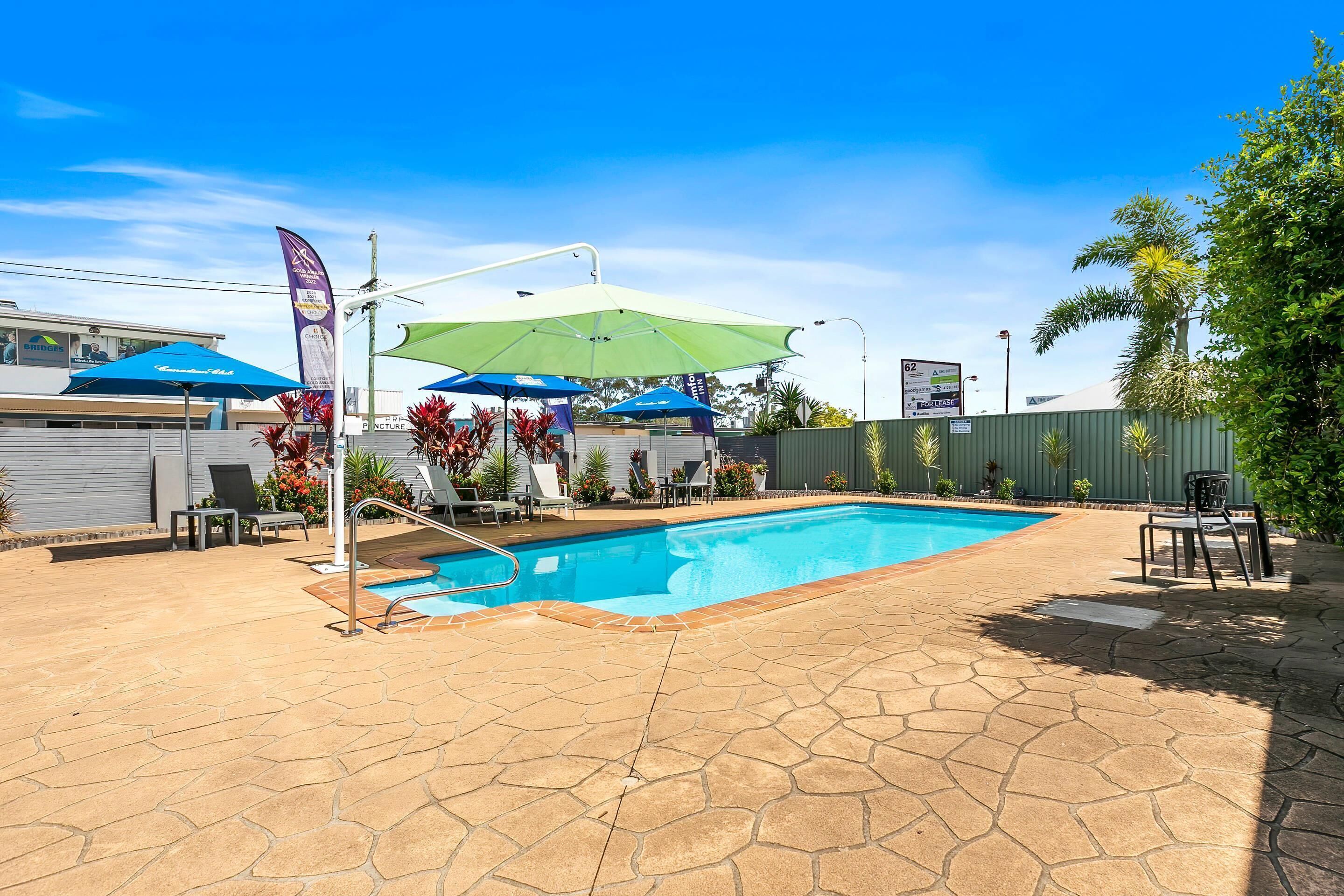 En swimmingpool med fliseterrasse, omgivet af liggestole og parasoller.