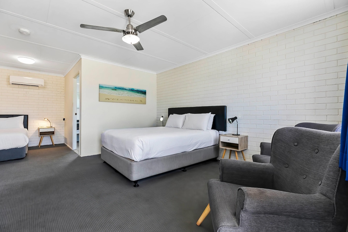 A hotel room with a bed, a chair, a desk, and a ceiling fan.