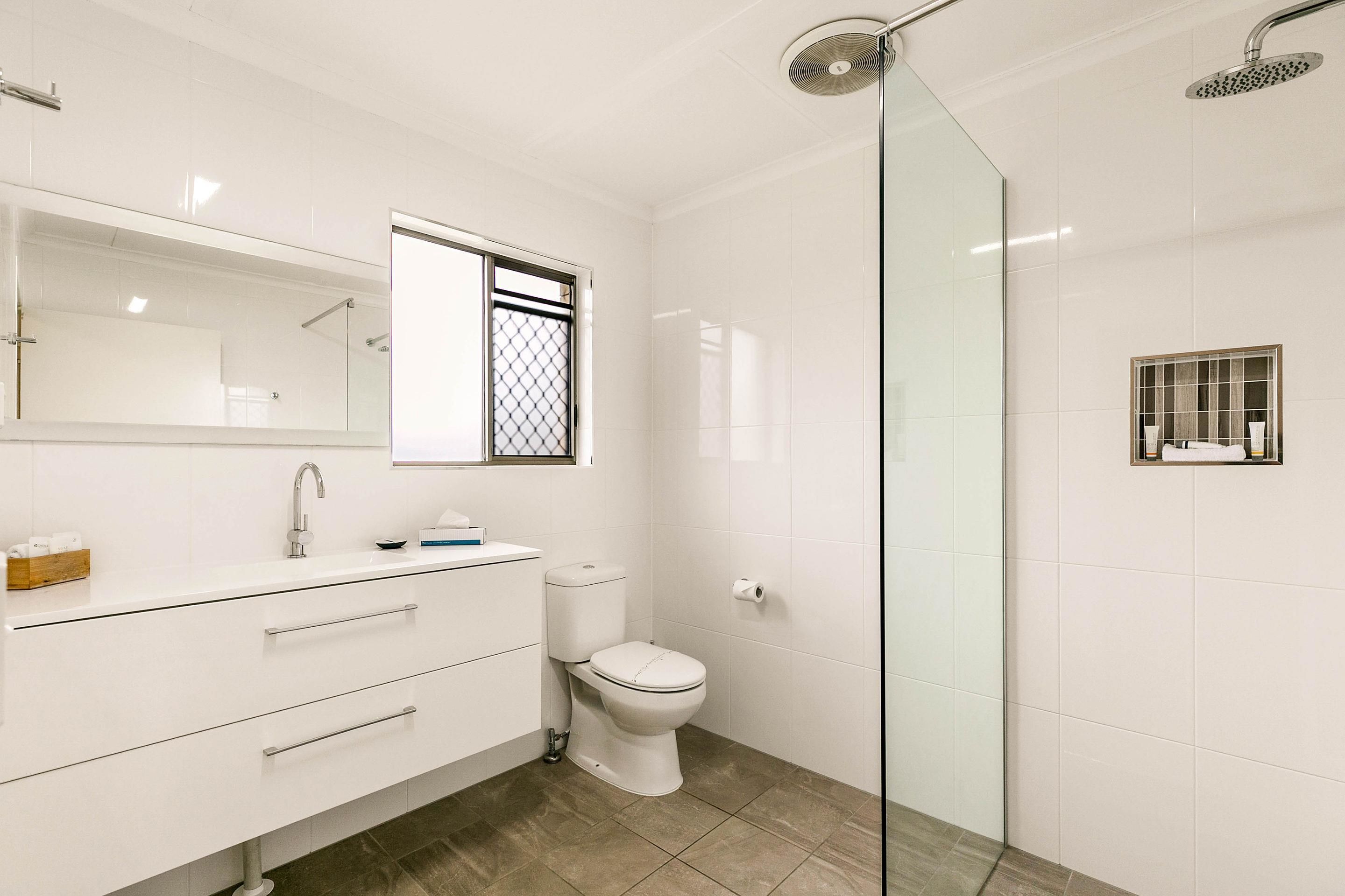 Un baño moderno con cabina de ducha de vidrio, inodoro, lavamanos con espejo y una ventana pequeña.