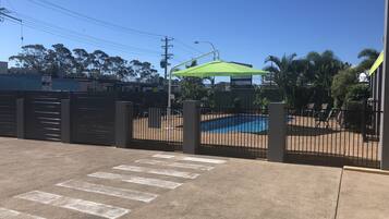 A gated area with a pool, a pedestrian crossing, and a green umbrella.