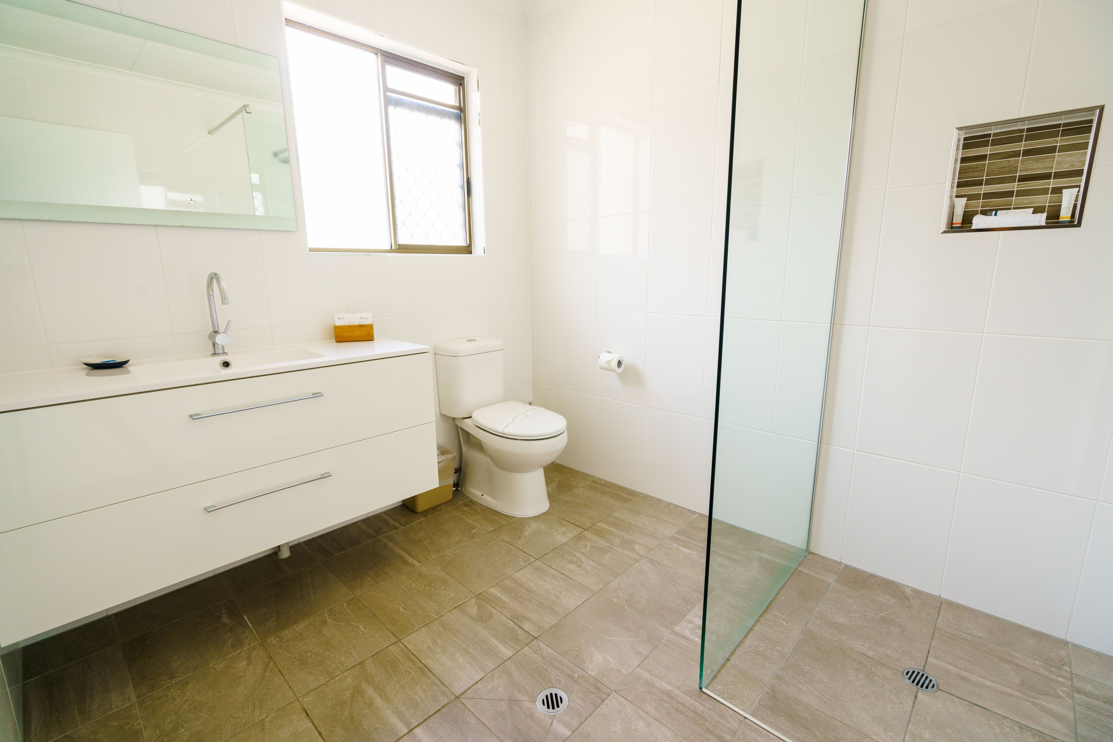 A modern bathroom with a glass shower enclosure, a white sink with a mirror above, and a toilet.