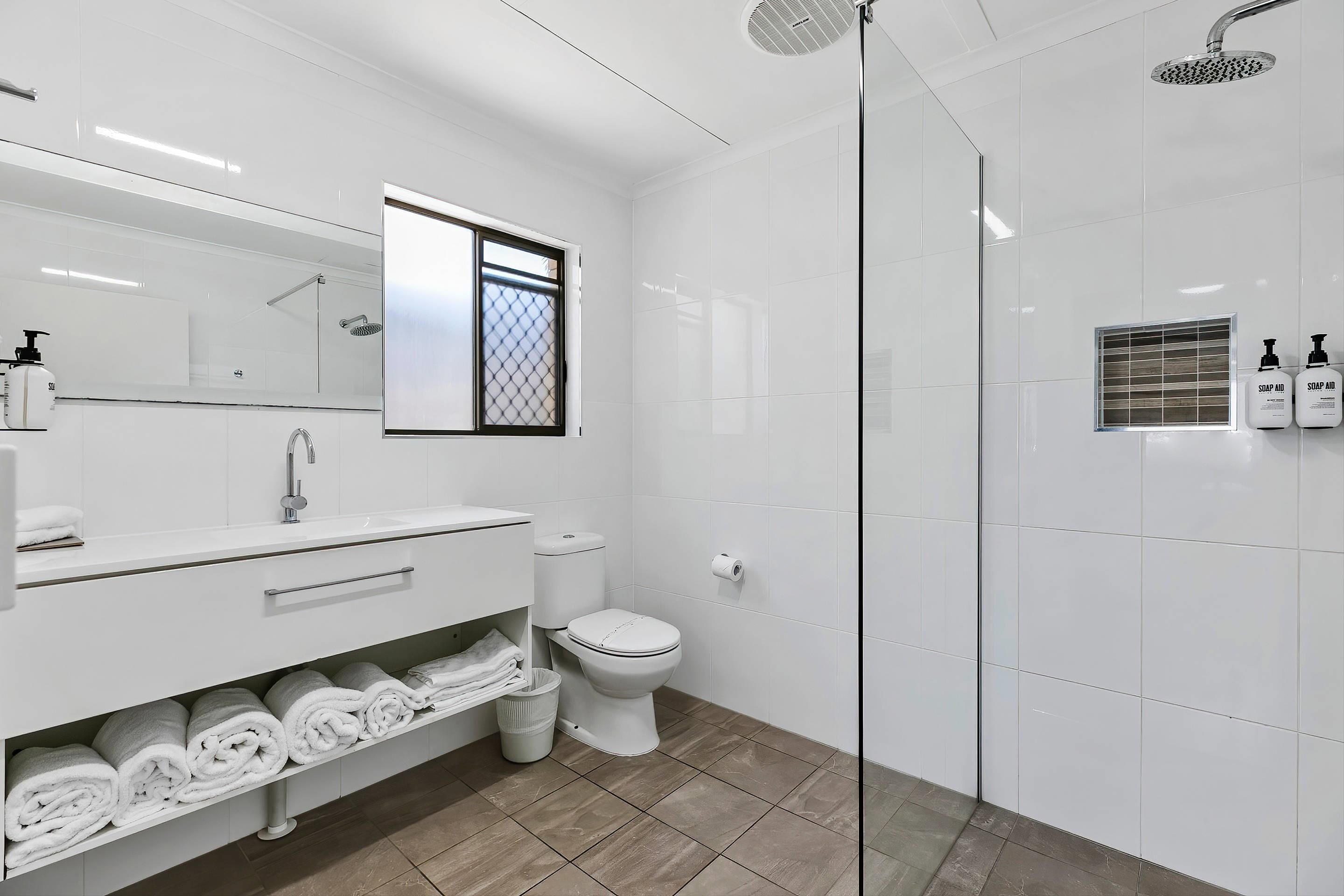 A modern bathroom with a glass-enclosed shower, a white vanity with towels, and a toilet.