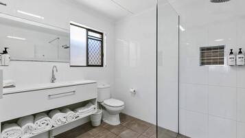 A modern bathroom with a glass-enclosed shower, a white vanity with towels, and a toilet.