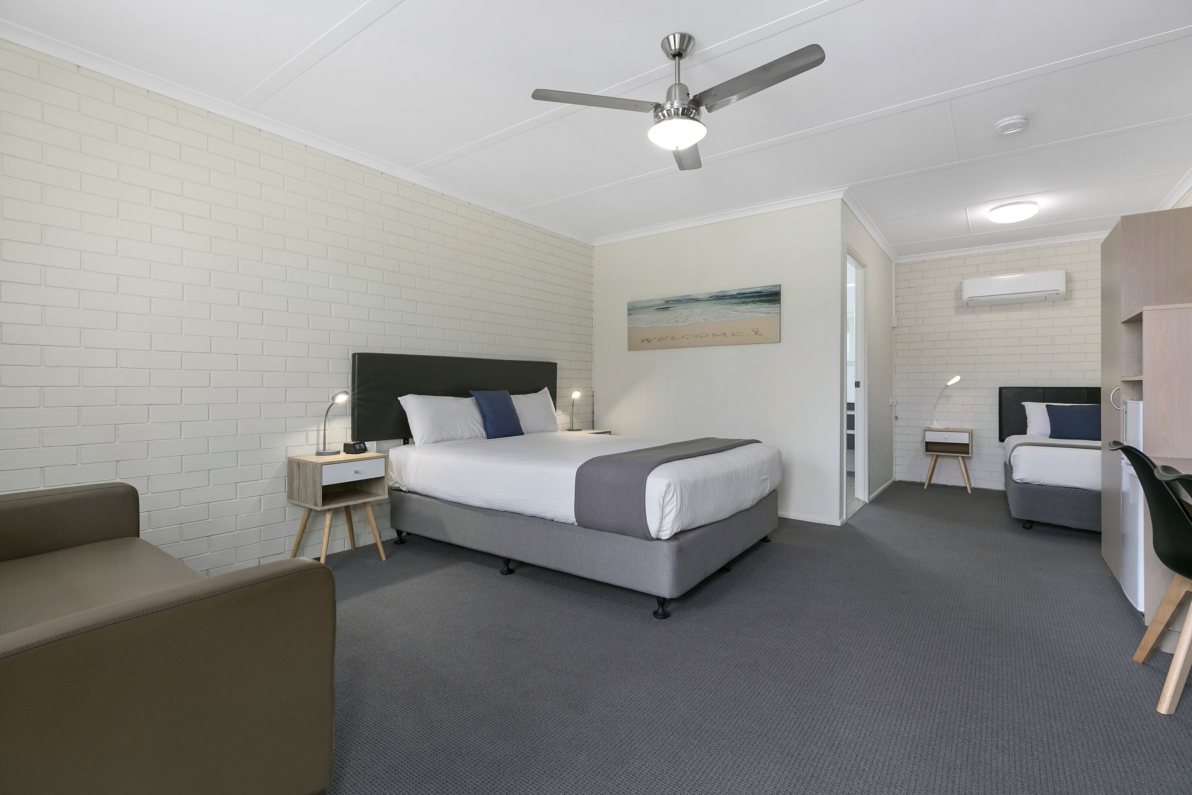 A hotel room with a bed, bedside table, chair, and a ceiling fan.
