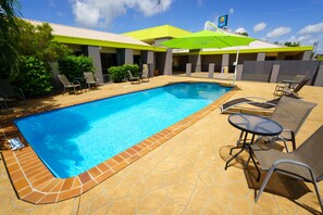 Uma piscina com espreguiçadeiras e uma mesa, cercada por um terraço revestido de azulejos.
