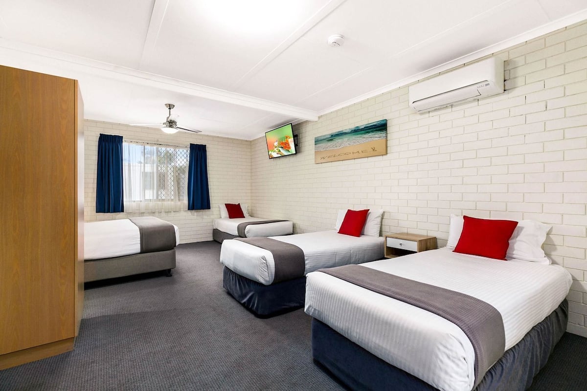 A hotel room with three beds, a TV, a ceiling fan, and a brick wall.