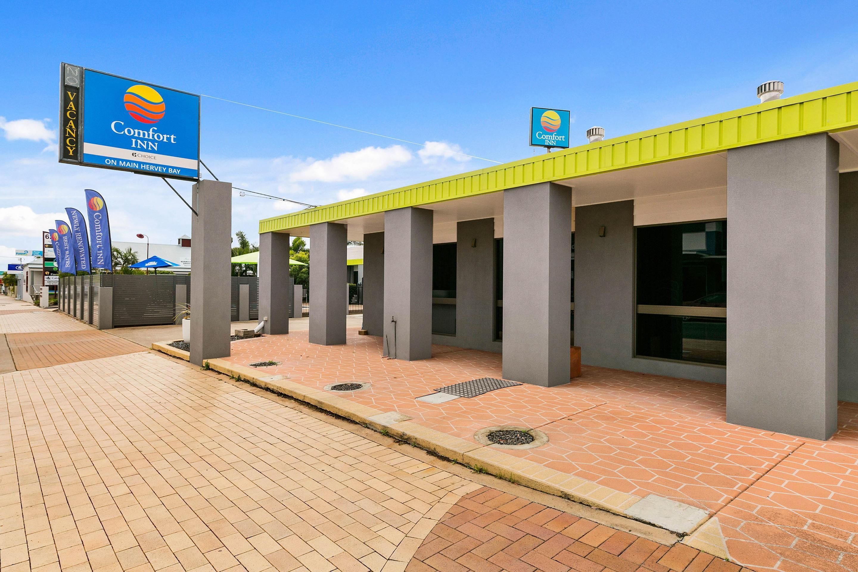 A Comfort Inn hotel with a clear sign indicating vacancy. The building has a modern design with a yellow roof and grey pillars.