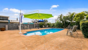 A swimming pool with a stone patio, a green umbrella, and outdoor furniture.