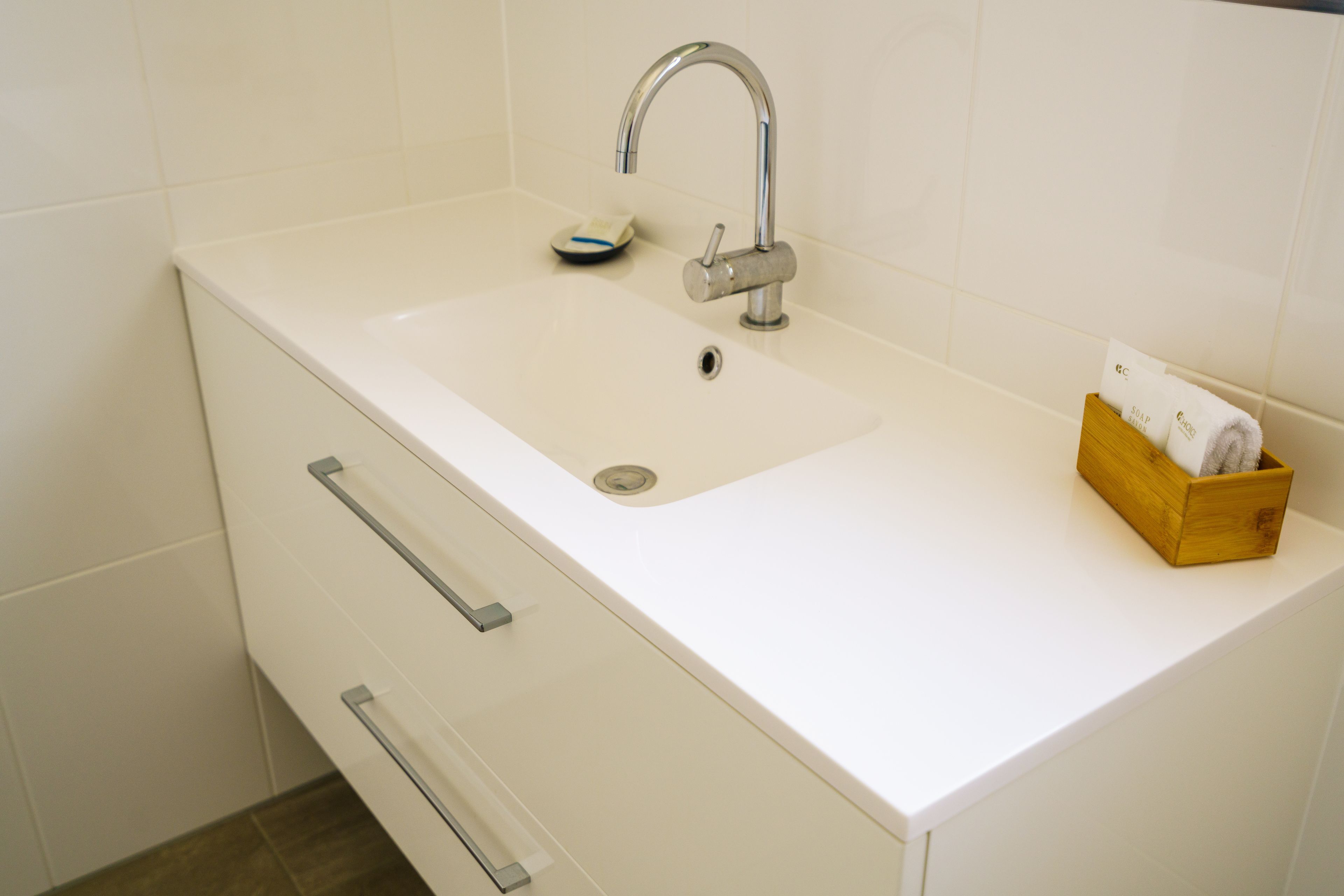 A white bathroom sink with a modern faucet, a soap dish, and a wooden box with towels.