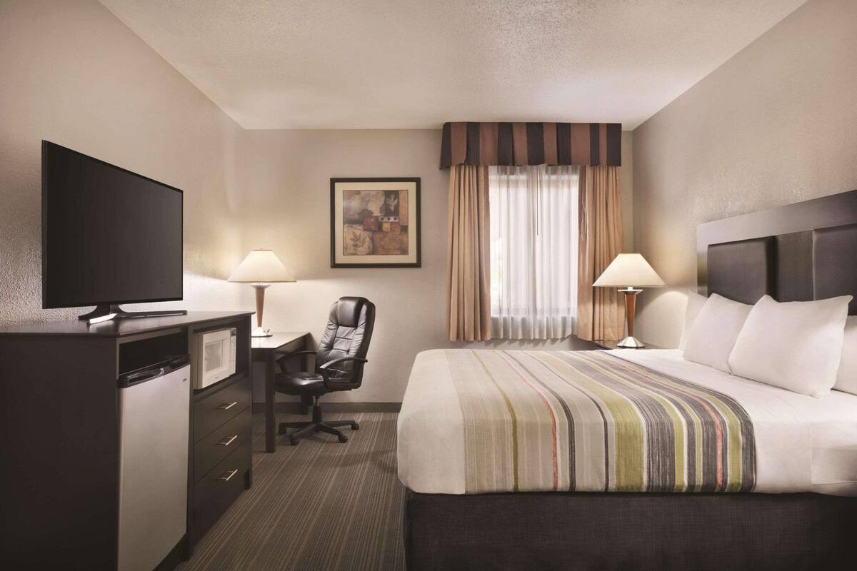 Ein Hotelzimmer mit einem Bett, einem Schreibtisch, einem Stuhl, einem Fernseher und einer Lampe.